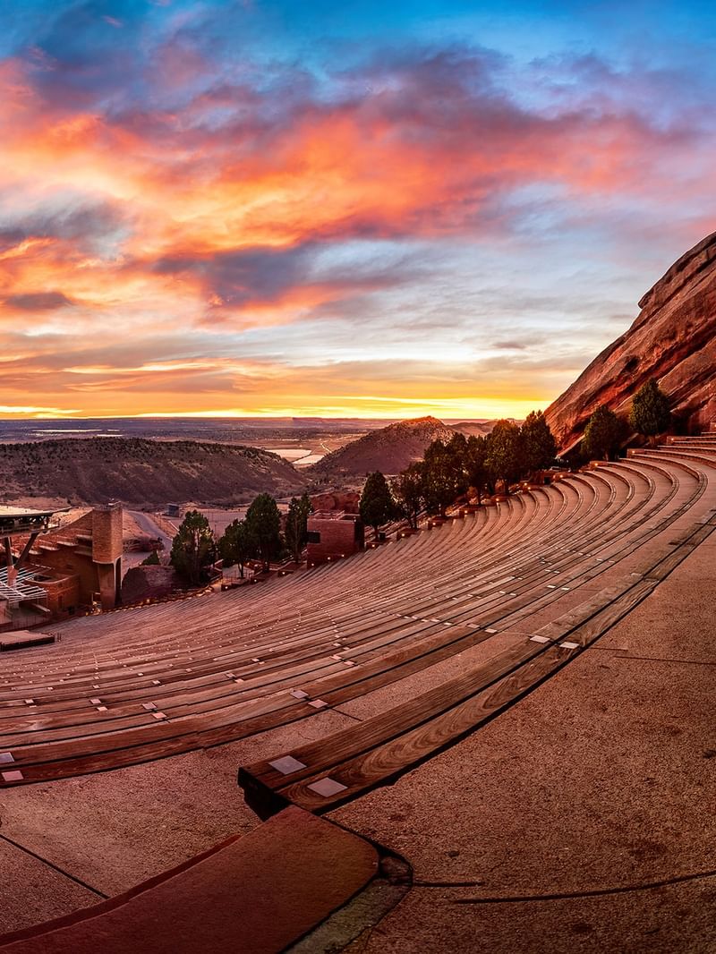 Red Rocks Amphitheatre with Stone benches by a rock formation under a vibrant sunset at an arena near Warwick Denver