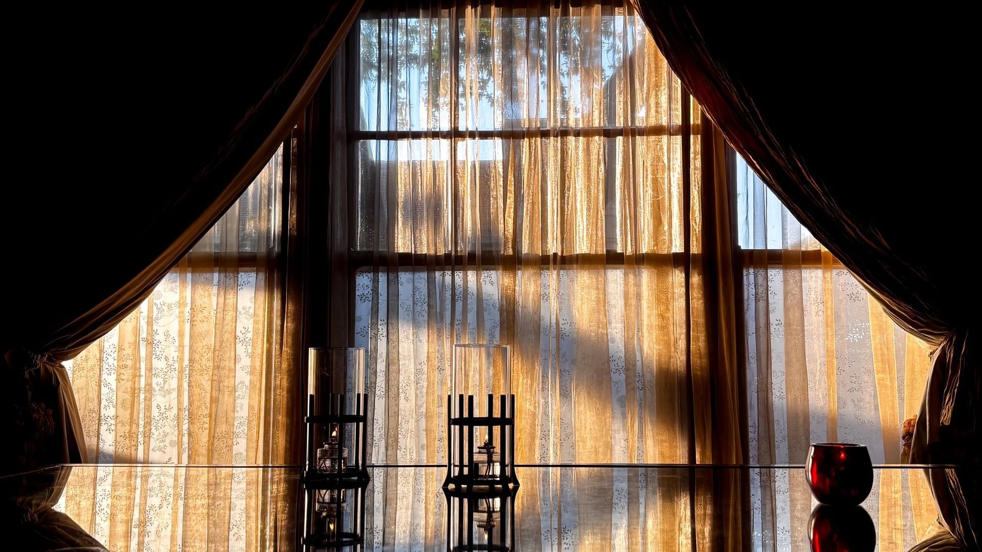 Glass candle holders by a dark table under a large window with gold curtains in The Library at Warwick Melrose Dallas