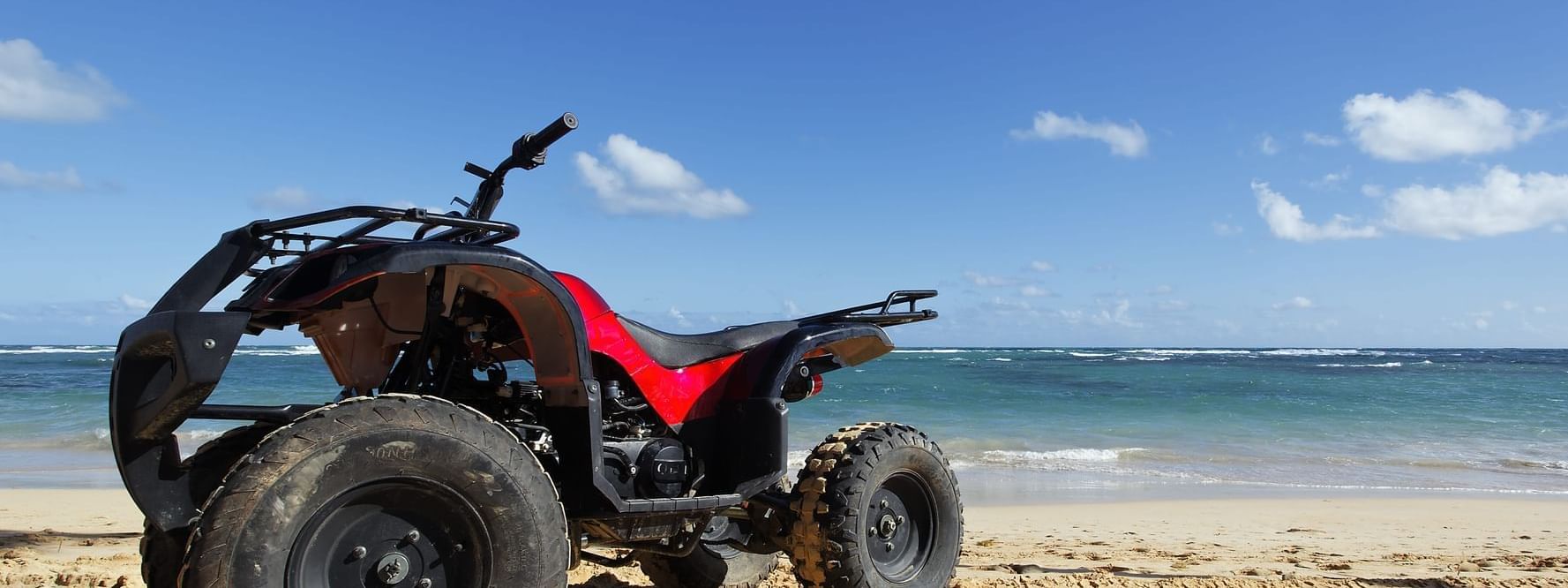 A red and black ATV parked on a sandy beach under a blue sky, near the Marquis Los Cabos Resort