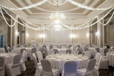 Round banquet tables with white tablecloths under decorative string lights in a ballroom at Rodd Charlottetown Hotel