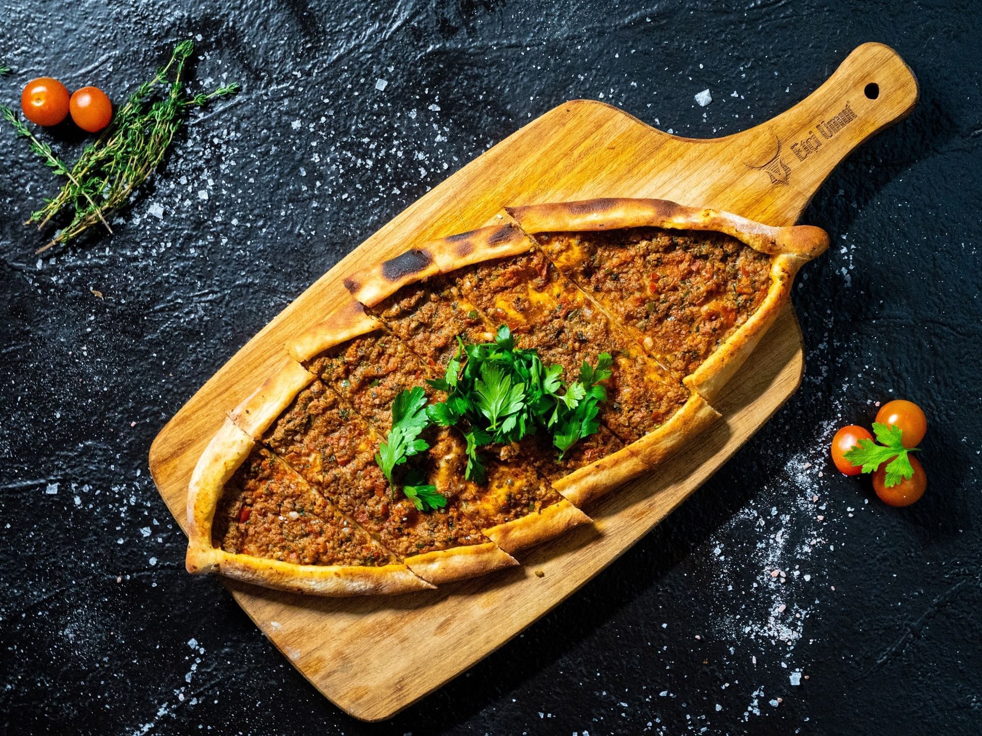 Turkish pide with minced meat topping, served on wooden board with herbs in Restaurant and Lounge at DAMAC Maison Aykon City