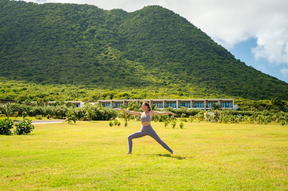 Vrouw die yoga beoefent in krijgerhouding op een groen gazon, met een majestueuze berg nabij Golden Rock Resort