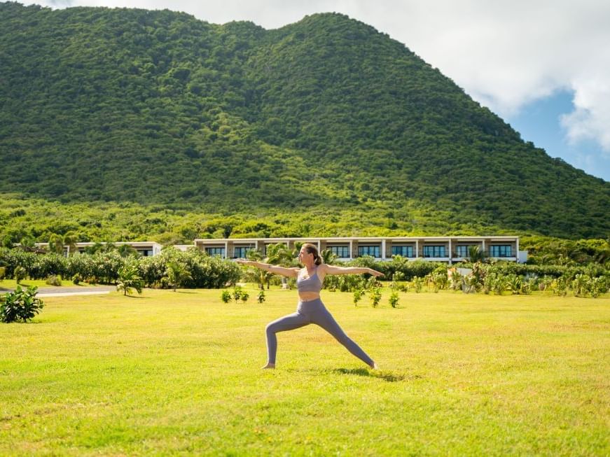 Woman practicing yoga in a warrior pose on a lush green lawn, with a majestic mountain near Golden Rock Resort