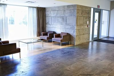 Lounge area with brown armchairs and a glass table by a window, and tile floors at the Schulich School of Business.