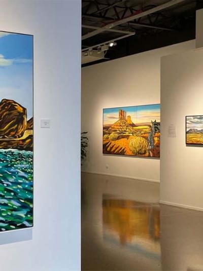 An art gallery interior with colorful landscape paintings displayed on white walls near Sofitel Brisbane Central