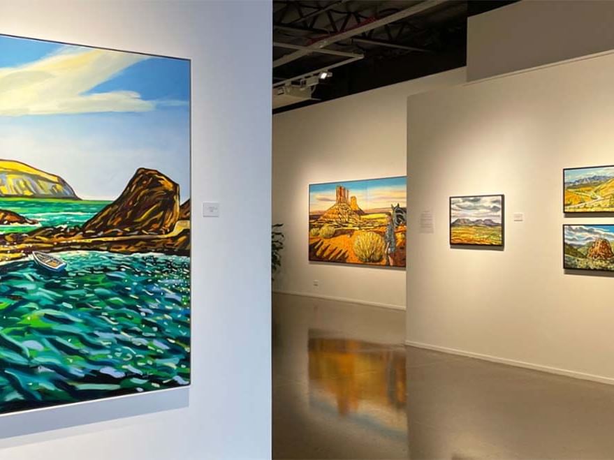 An art gallery interior with colorful landscape paintings displayed on white walls near Sofitel Brisbane Central