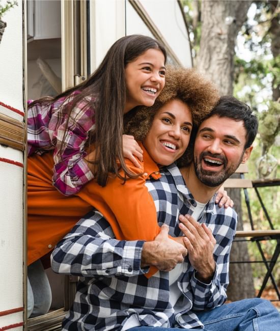 Family of three hugging and laughing together in front of the camper van at Fall Creek Marina & Campground