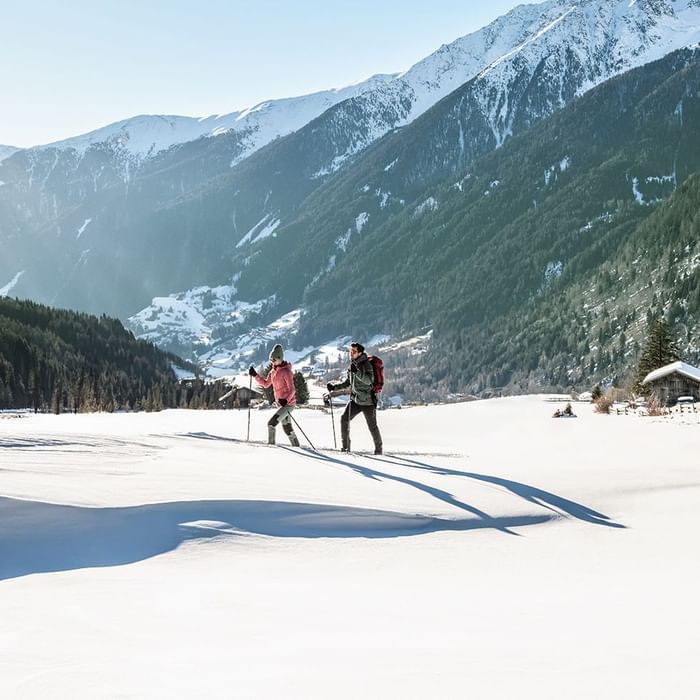 A couple walking with ice skating equipment in a snowy landscape near Falkensteiner Hotel Antholz