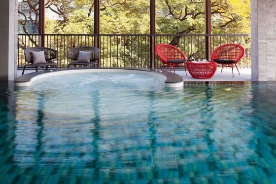 Indoor pool with comfy chairs and outdoor view at Eastin Tan Hotel Chiang Mai