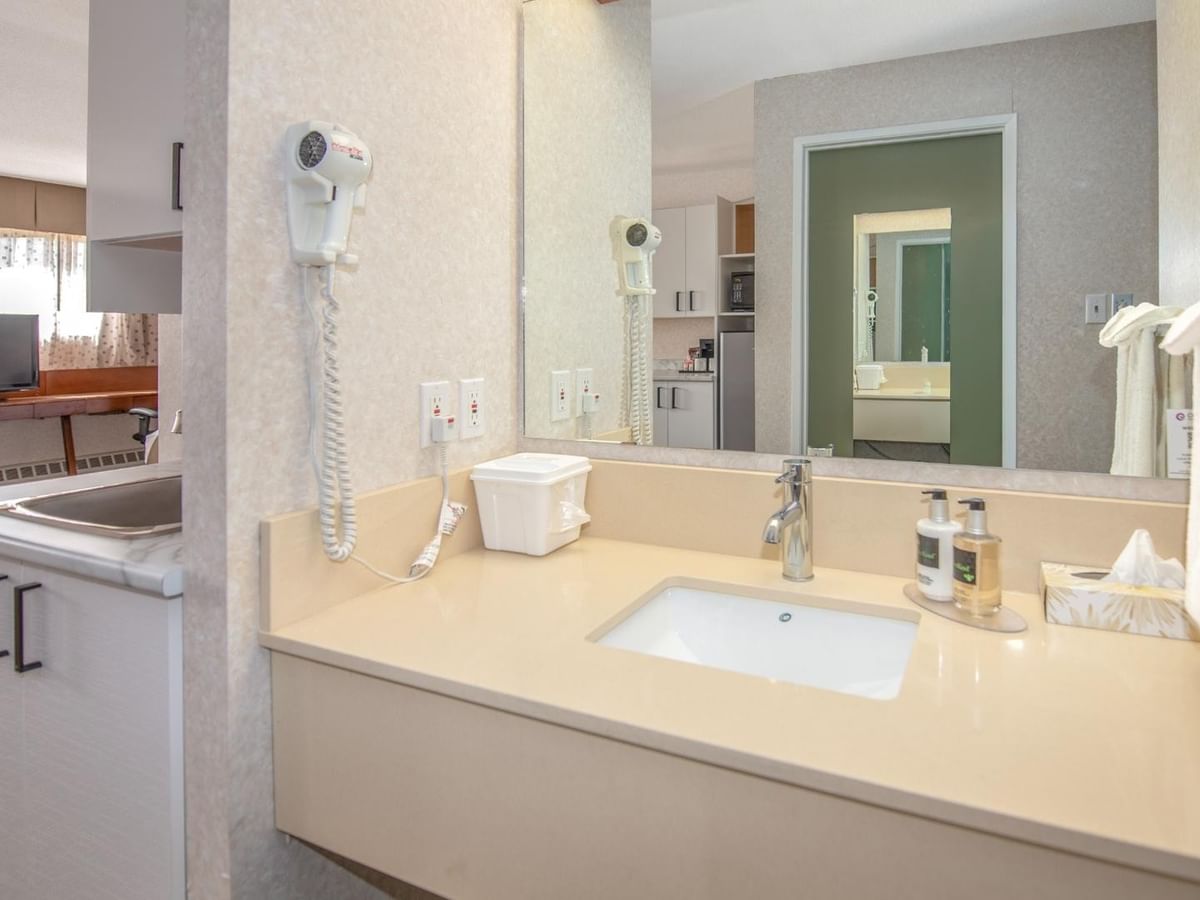 A bathroom with a sink, mirror, towel rack, and a room visible through the mirror.