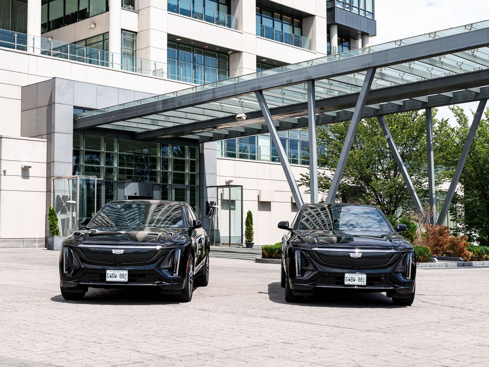 Two black luxury SUVs at the Hotel X Toronto entrance, featuring a modern glass-and-steel canopy over the main driveway