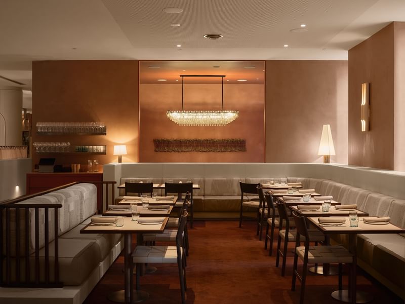 An elegant restaurant with wooden floors, brown walls, cushioned benches, and tables set with white plates and glasses.