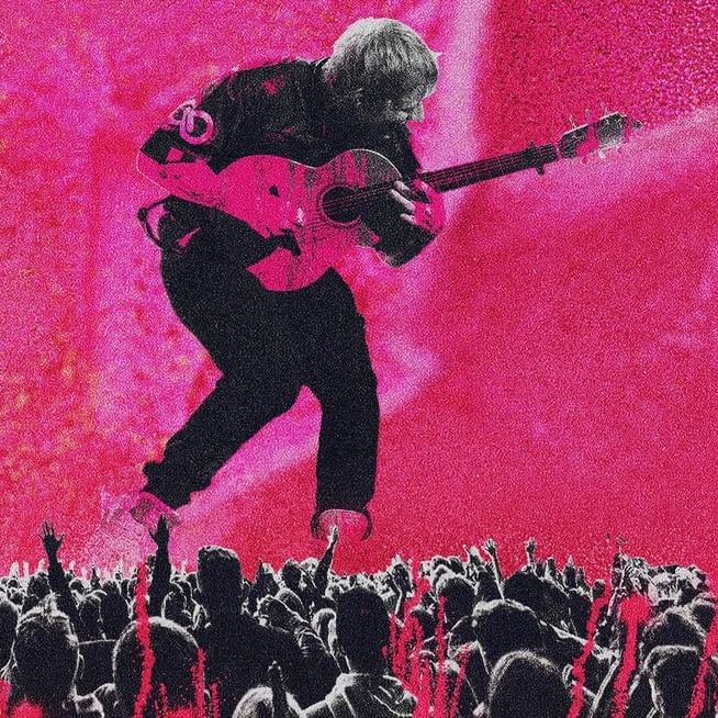 Ed Sheeran performing live on stage with a guitar at a concert.