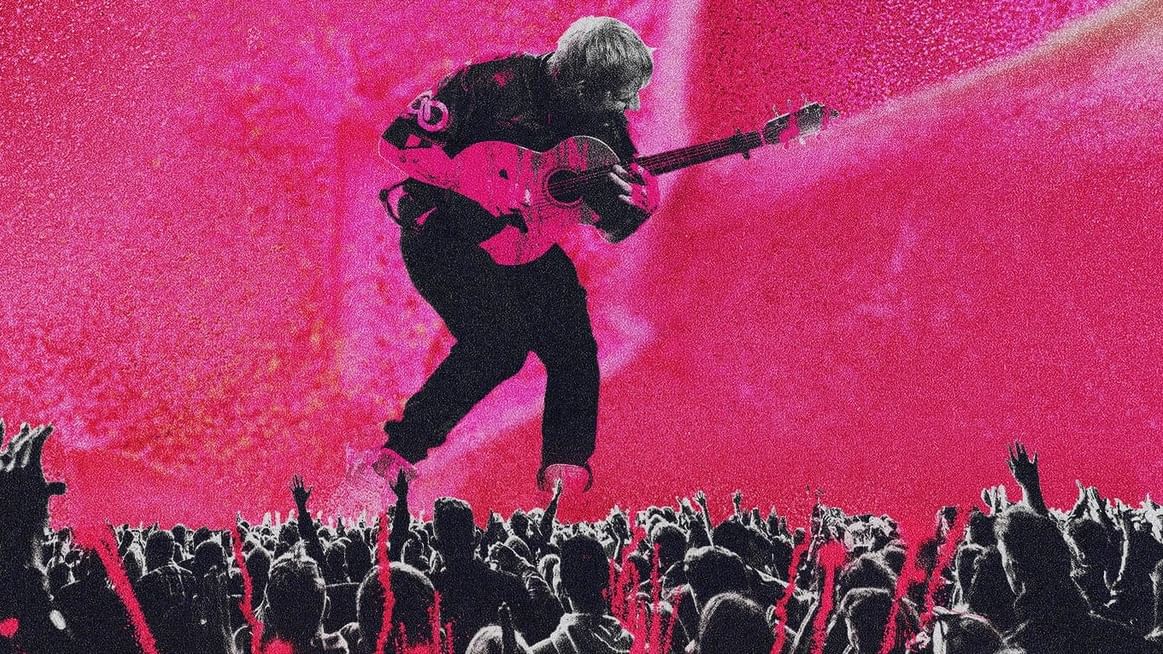 Ed Sheeran performing live on stage with a guitar at a concert.