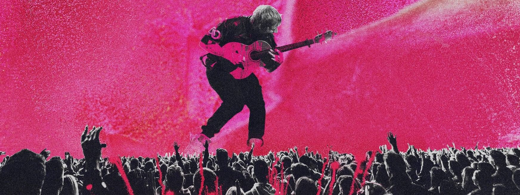 A musician performs on stage with a guitar in front of a crowd with a pink background.