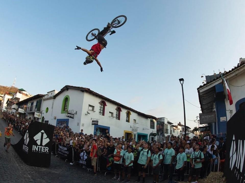 BMX rider performing a flip in midair with a crowd watching during the Puerto Vallarta Downhill event.