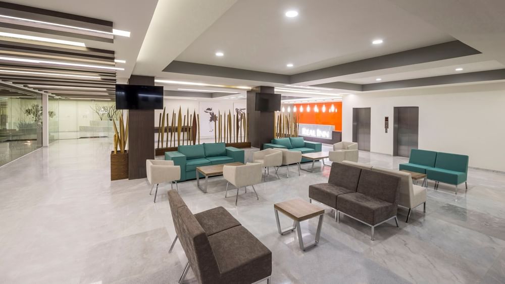 Spacious lobby with teal and brown seating, marble floors, and decorative wood pillars at Real Inn Celaya
