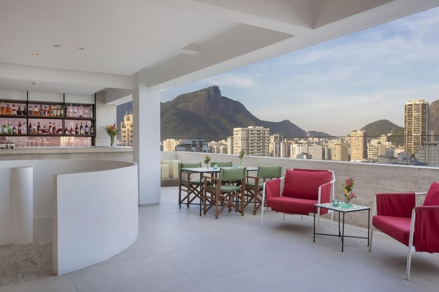 Bar rooftop do Janeiro Hotel com linda vista da zona sul do Rio de Janeiro e do corcovado decorado com mesas e cadeiras verde e poltronas vermelhas