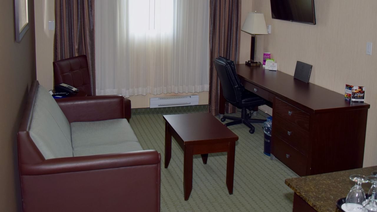 A hotel room with a couch, desk, chair, TV, lamp, and window with curtains.