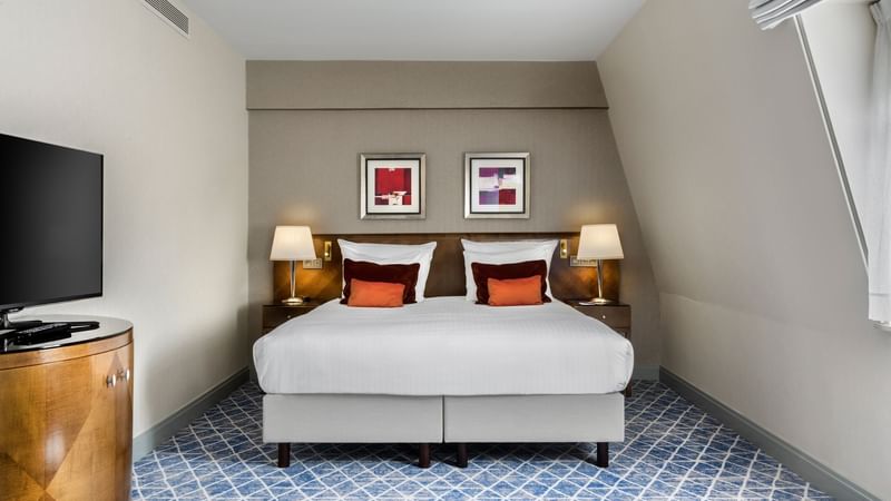 Bed area with nightstand and paintings on the wall in Premium Deluxe Room at Warwick Brussels