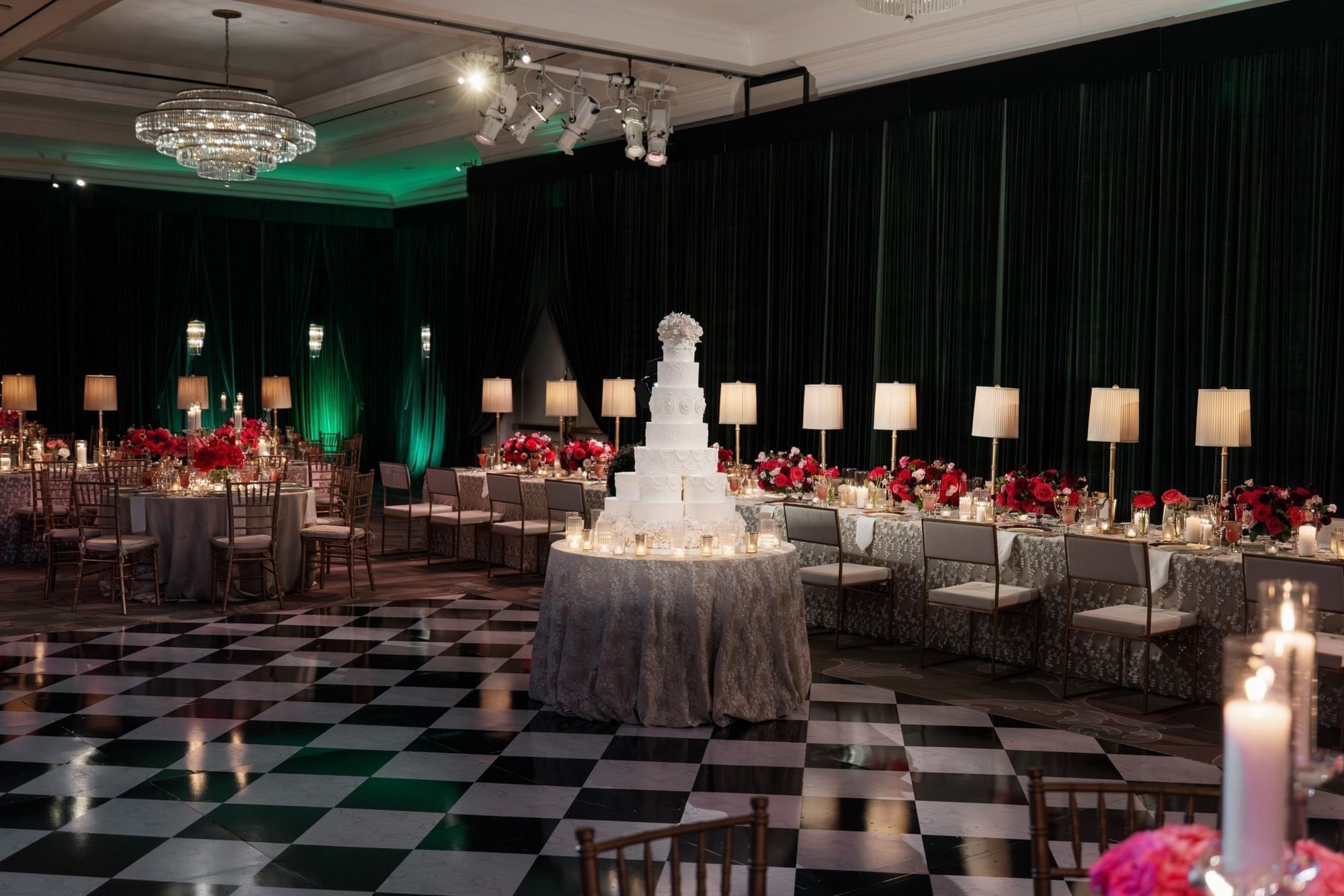 Tiered wedding cake on a round table by long dining setups under a dark green drape at Warwick Melrose Dallas