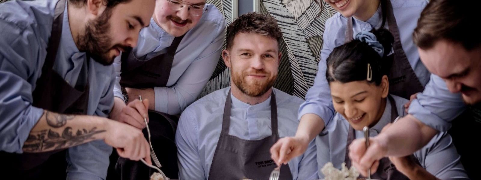 Tom Brown and team sharing a meal at a table, celebrating Michelin Star achievement.