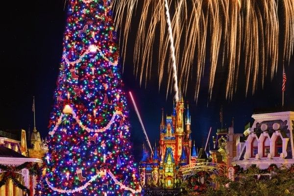 A sparkling Christmas tree with fireworks bursting over a colorfully lit Cinderella Castle at Magic Kingdom during the Disney Christmas party.