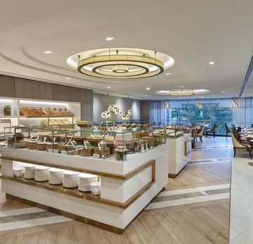 A large buffet hall with glass displays, stacks of plates, and a central circular light fixture in Alesta Restaurant at Titanic Port Bakırköy