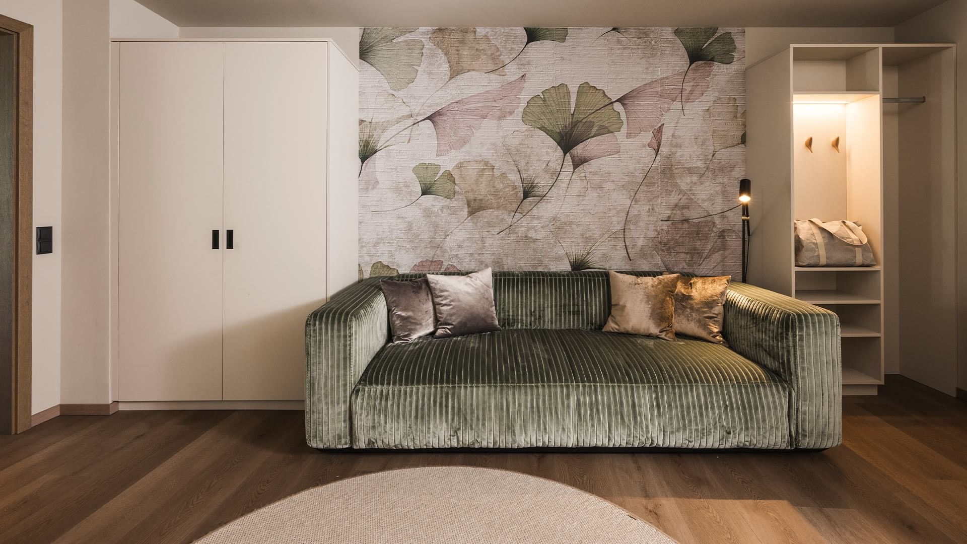 Modern room with green velvet couch, leaf-patterned wall, and white storage units.