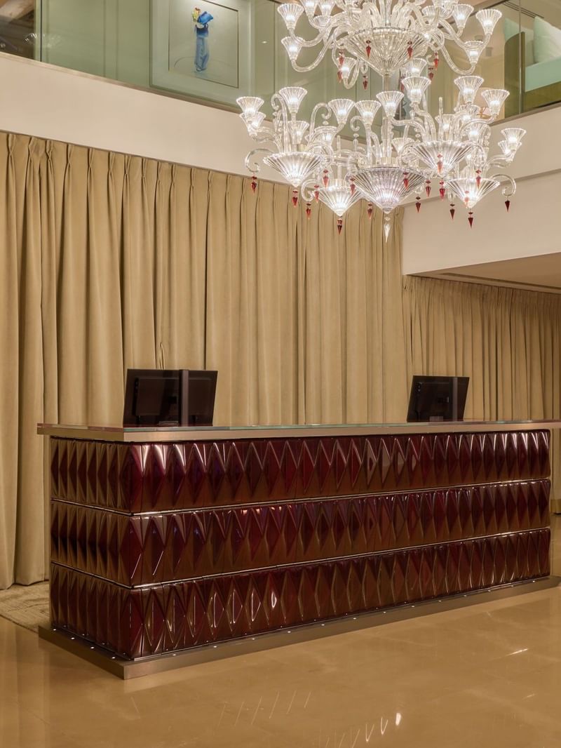 Concierge desk at The May Fair Hotel under a large chandelier.