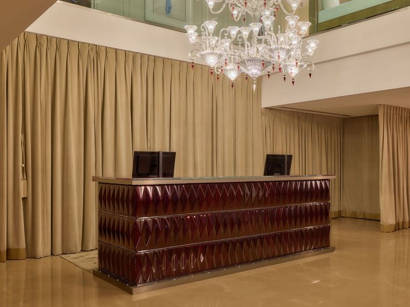 Concierge desk at The May Fair Hotel under a large chandelier.