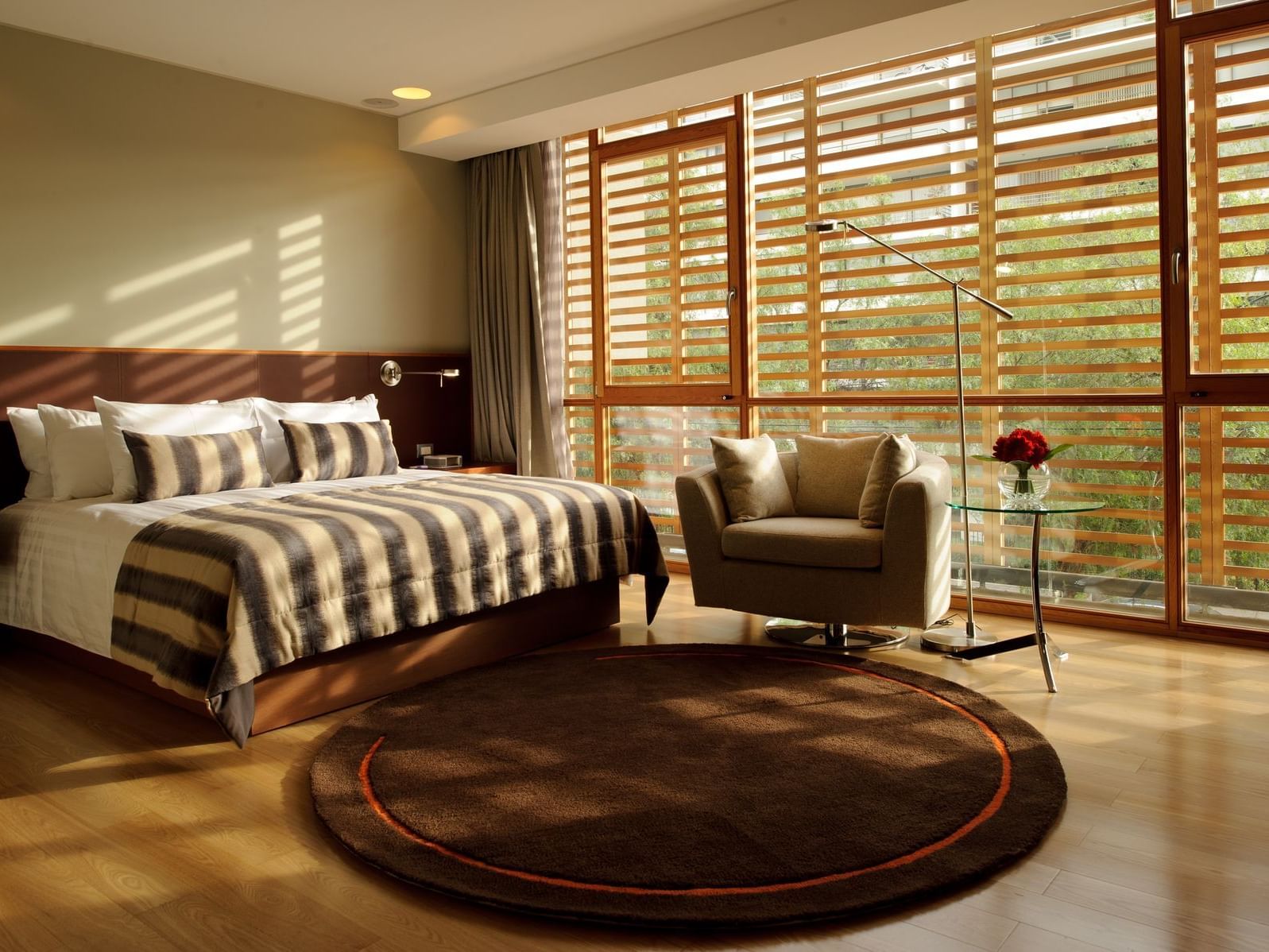 Quarto Deluxe 2 com cama king, poltrona bege, persianas de madeira e luz natural no NOI Vitacura em Vitacura