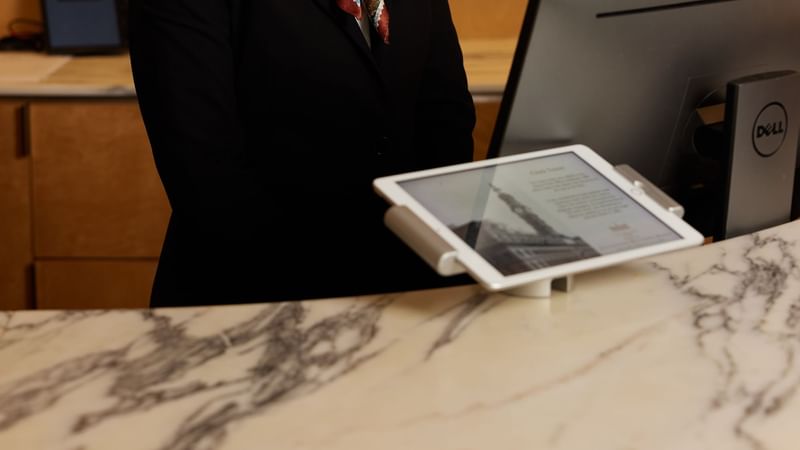 A person in a black suit standing near a counter with a tablet on it at Fullerton Hotel Sydney