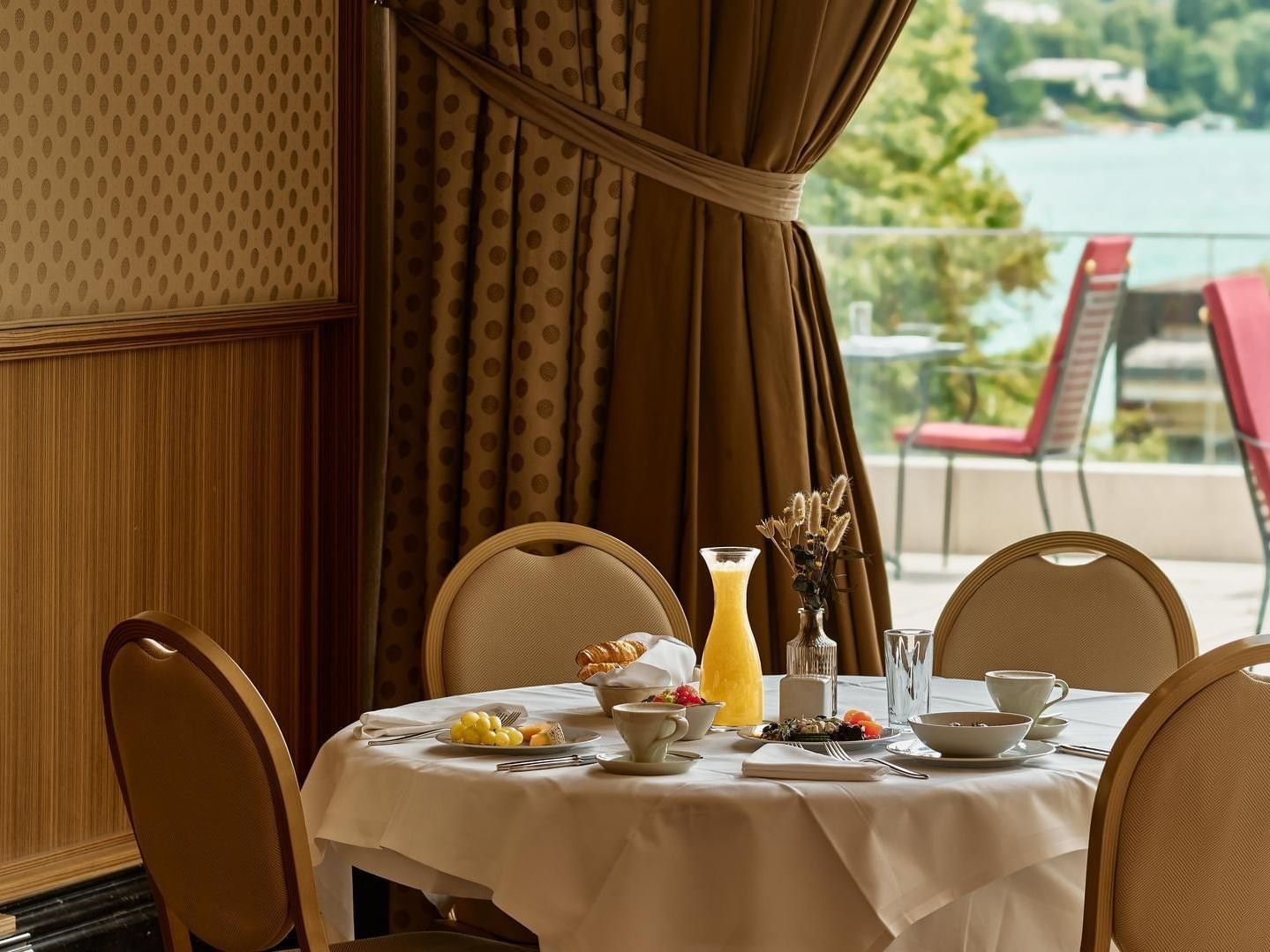 Sala da pranzo con tavoli imbanditi e vista su un lago attraverso finestre a vetrata.