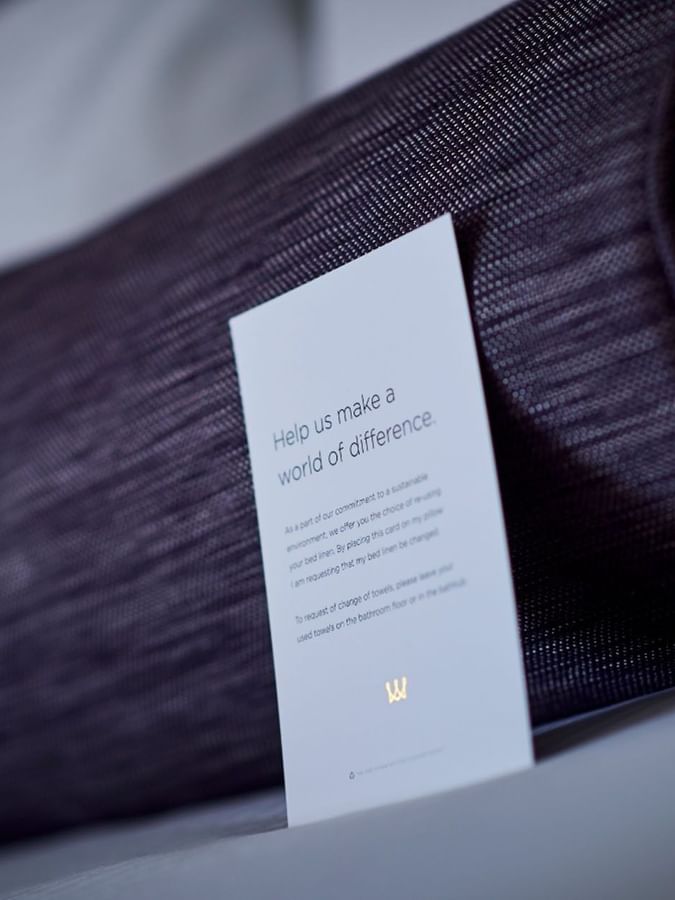 Sustainability card by a purple bolster pillow on a bed in Classic Rooms at Warwick Denver