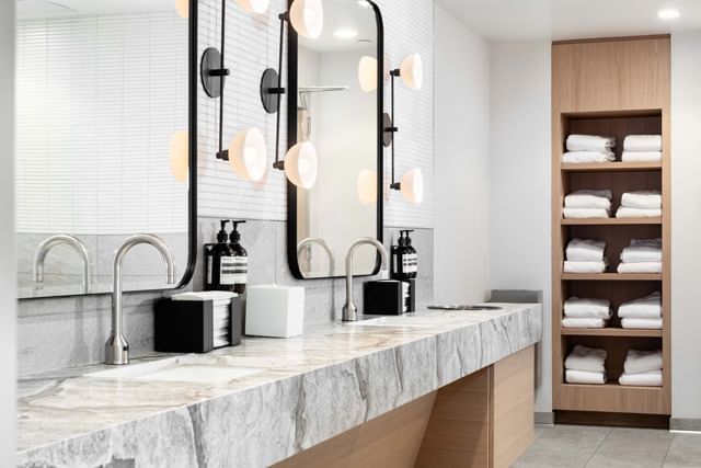 Hospitality Suite bathroom with a marble vanity and towels stacked on a wood shelf at the Maui Coast Hotel