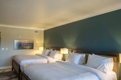 A cozy hotel bedroom at The Stanley Hotel with two beds, featuring a teal accent wall and a landscape art