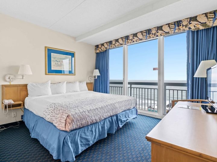 A wide-angle view of a hotel room with a double bed, desk, and ocean view.