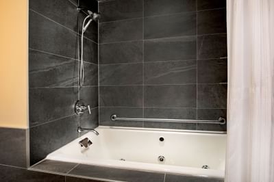 Bathtub with a handheld shower head against dark tile walls and a safety grab bar in the Suite at Harborside Inn Boston