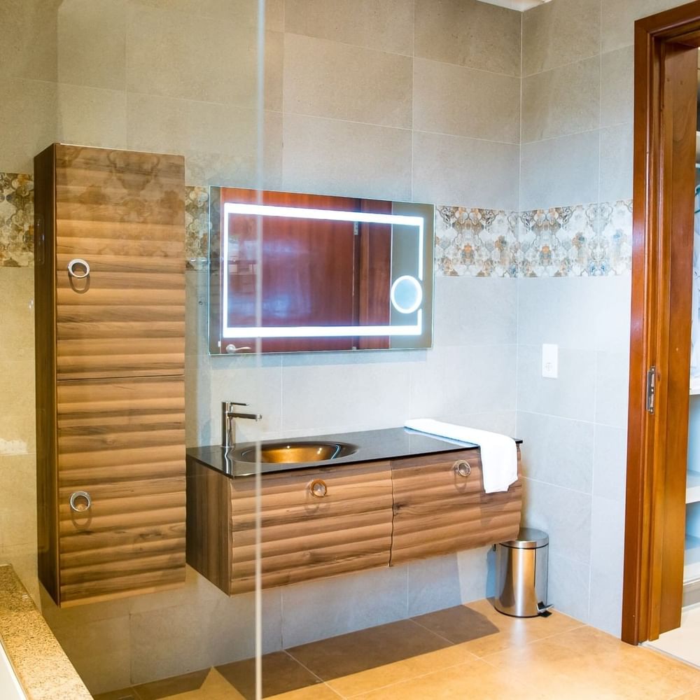 Elegant bathroom with wooden vanity, lighted mirror, and bathtub at Lake Victoria Serena Golf Resort & Spa in Kampala.