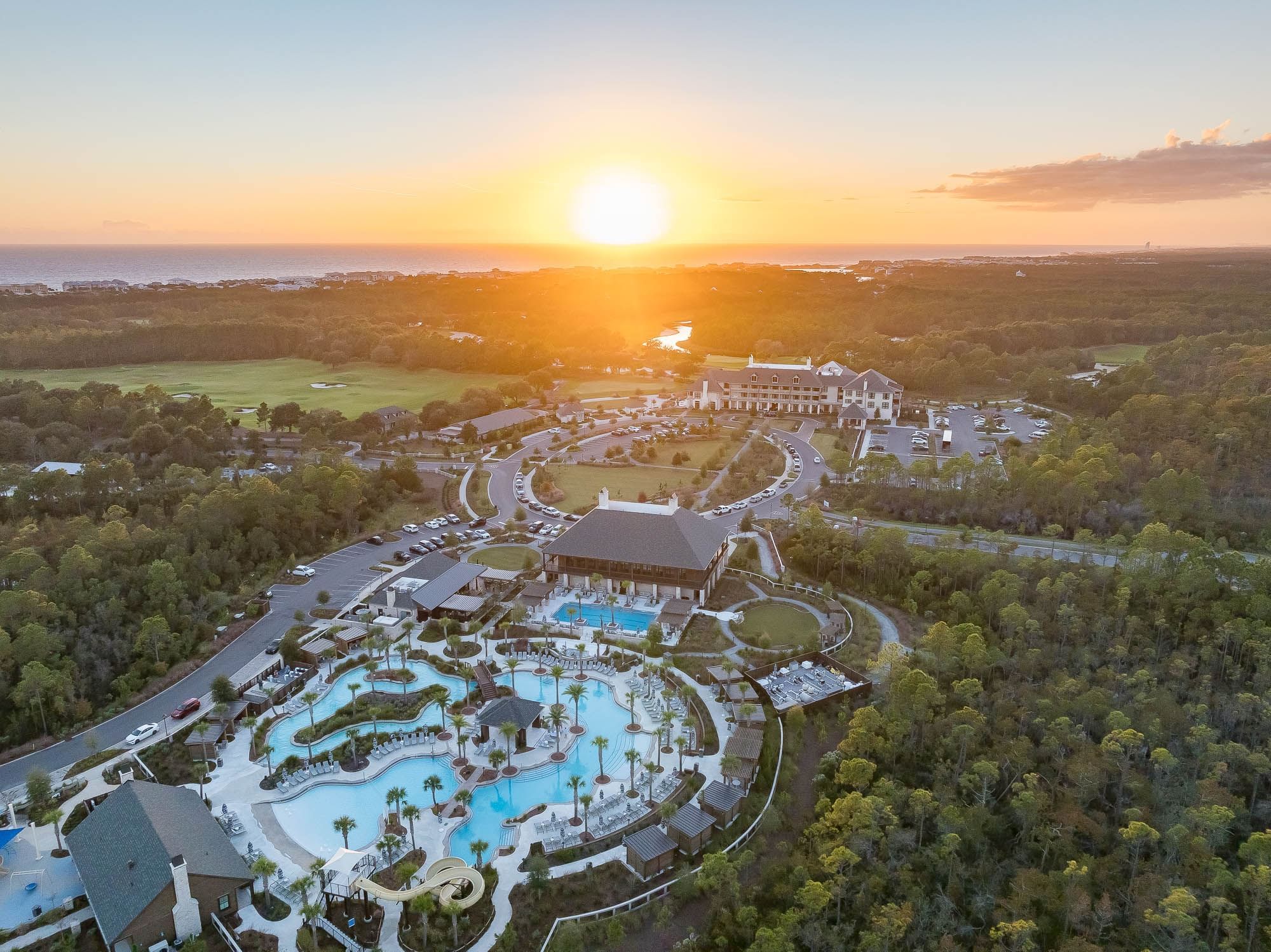 Aerial view of resort with pool and water slide at sunset with ocean in background.