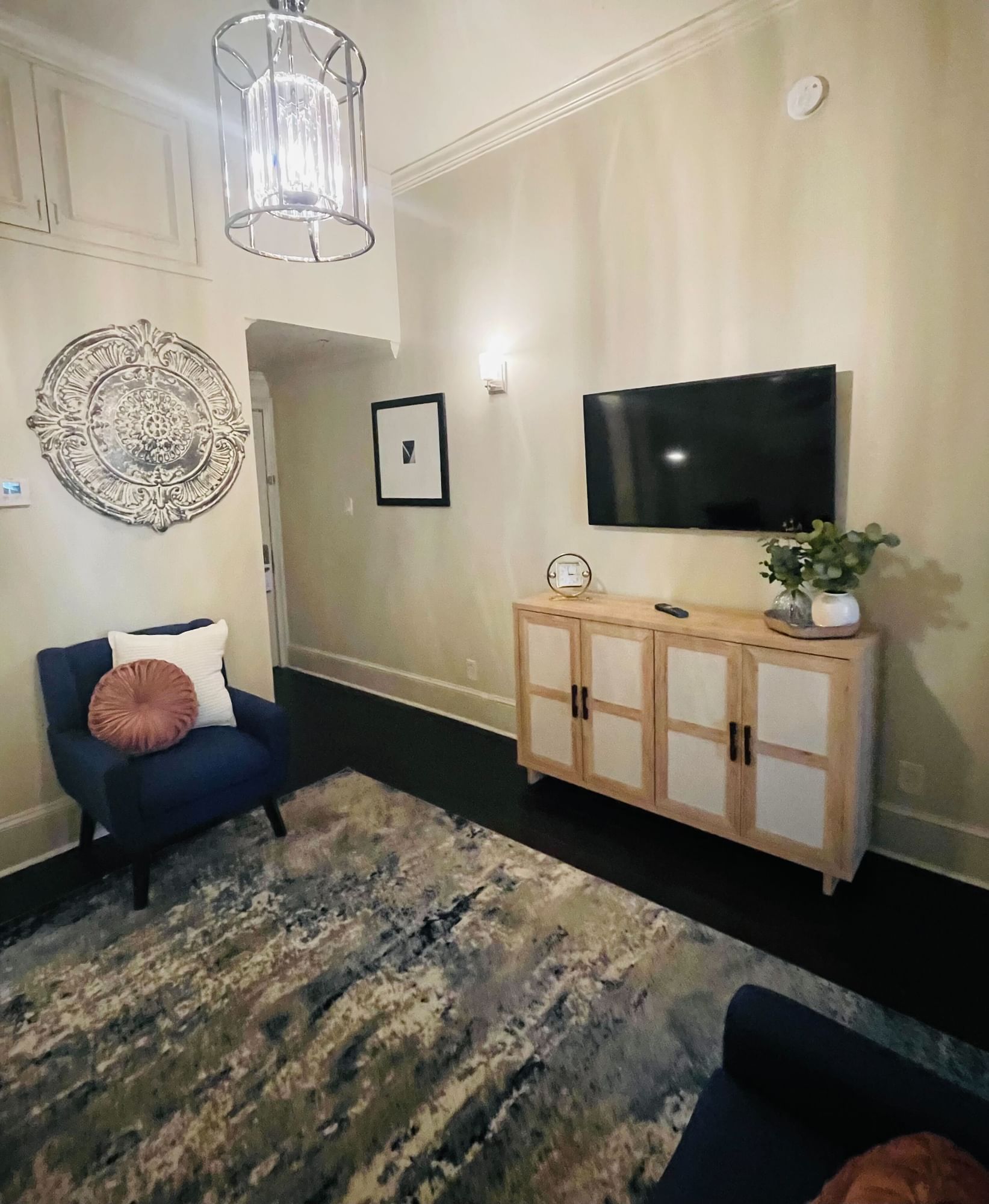 A wide view of a junior suite with a blue chair, a TV on a cabinet, and a patterned rug.