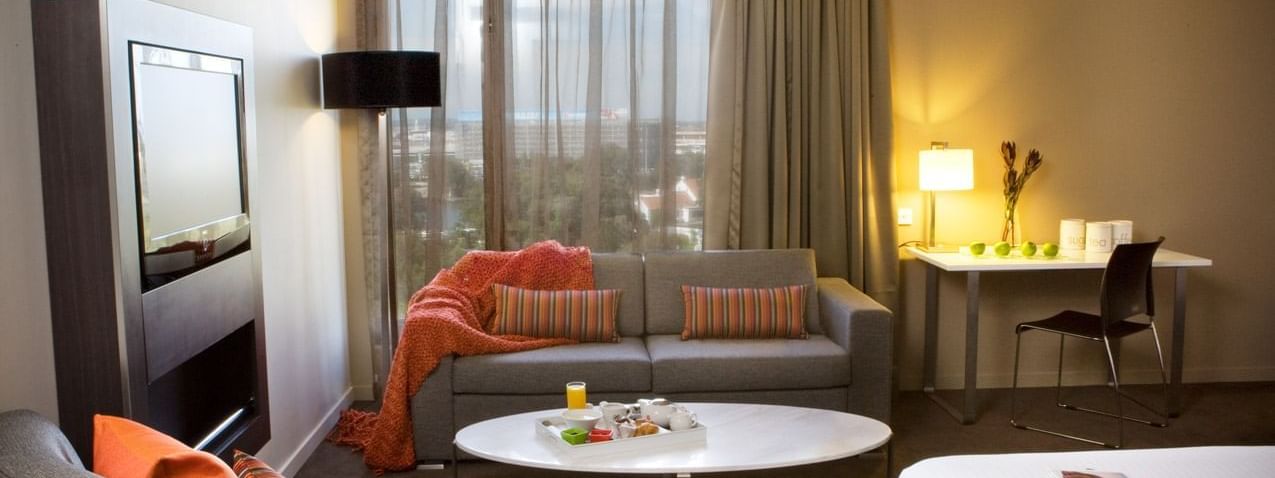 TV lounge with plush seating by the window and a work desk in Family Room at Novotel Sydney International Airport