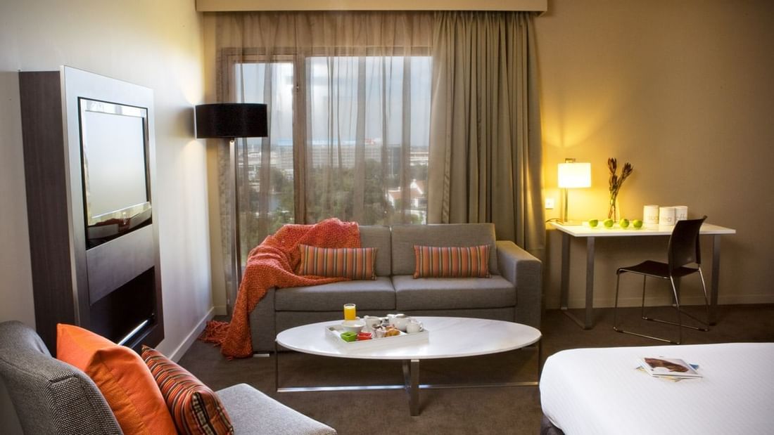 TV lounge with plush seating by the window and a work desk in Family Room at Novotel Sydney International Airport
