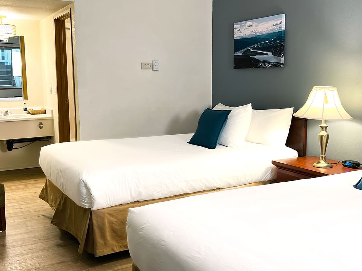 Hotel bedroom with two beds, lamp, night stand, paintings, and mirror