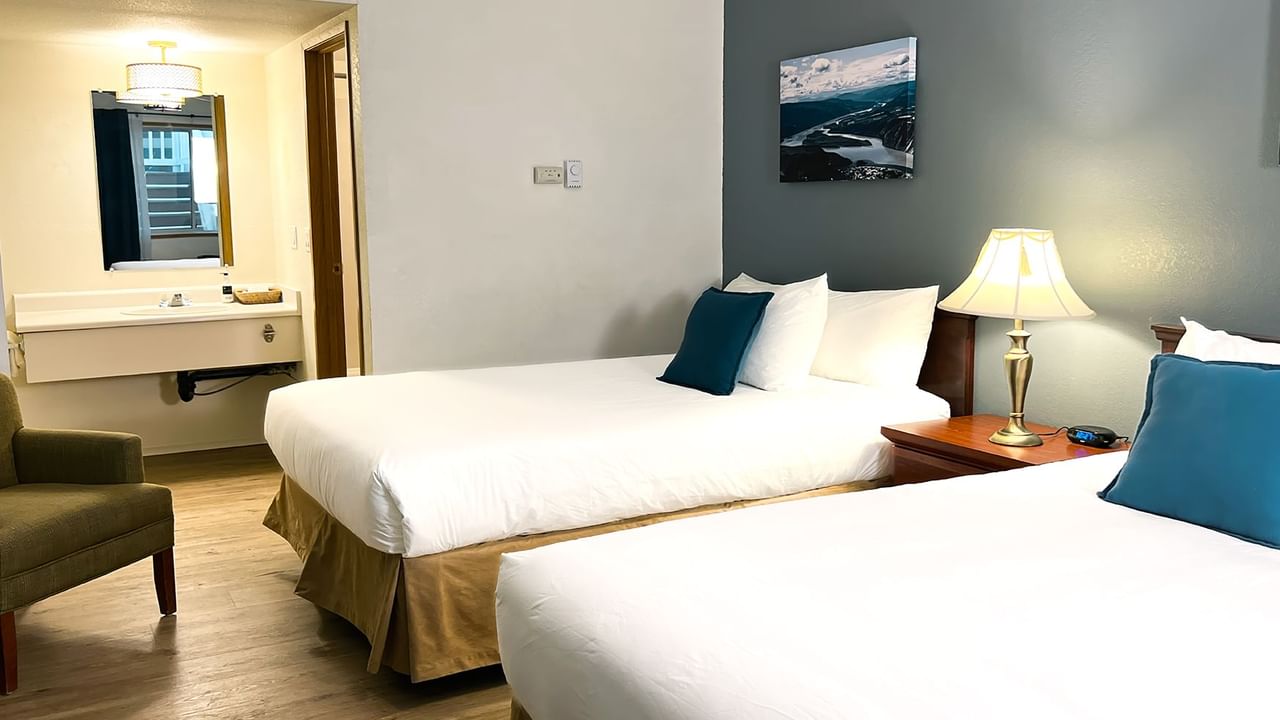 Hotel bedroom with two beds, lamp, night stand, paintings, and mirror