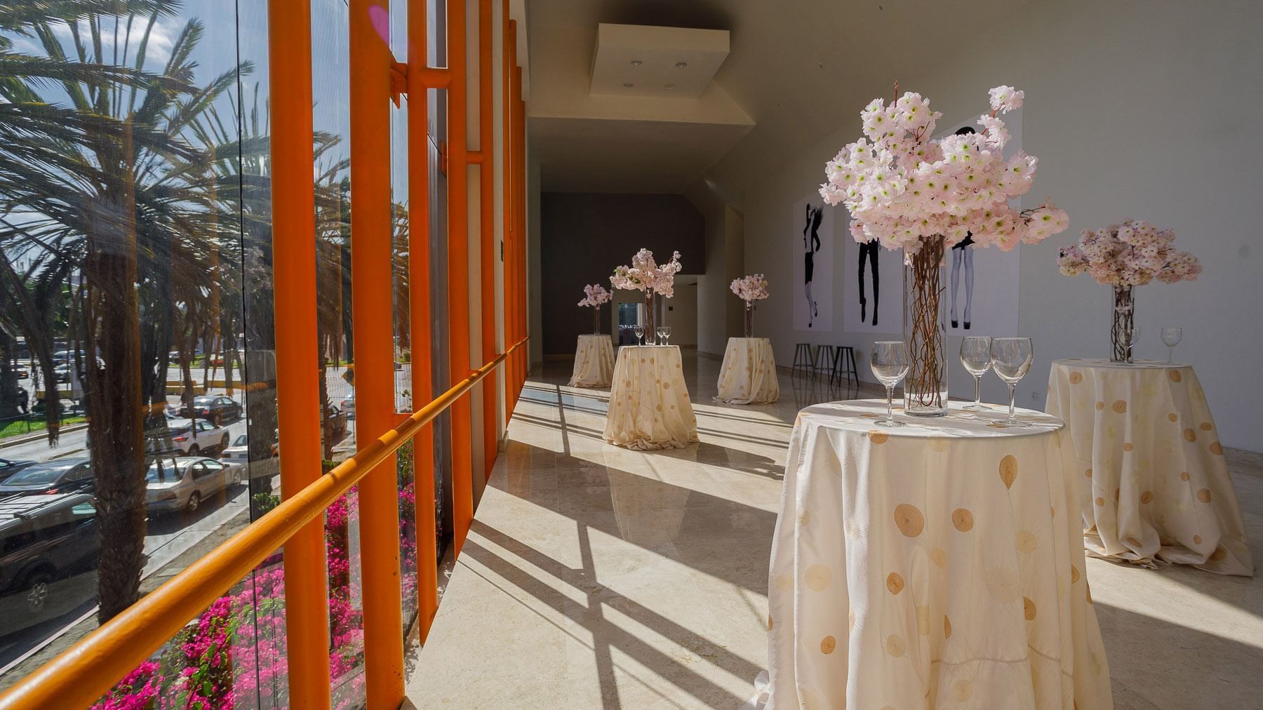 Sunlit hallway with tall floral arrangements and large windows overlooking palms at Real Inn Tijuana