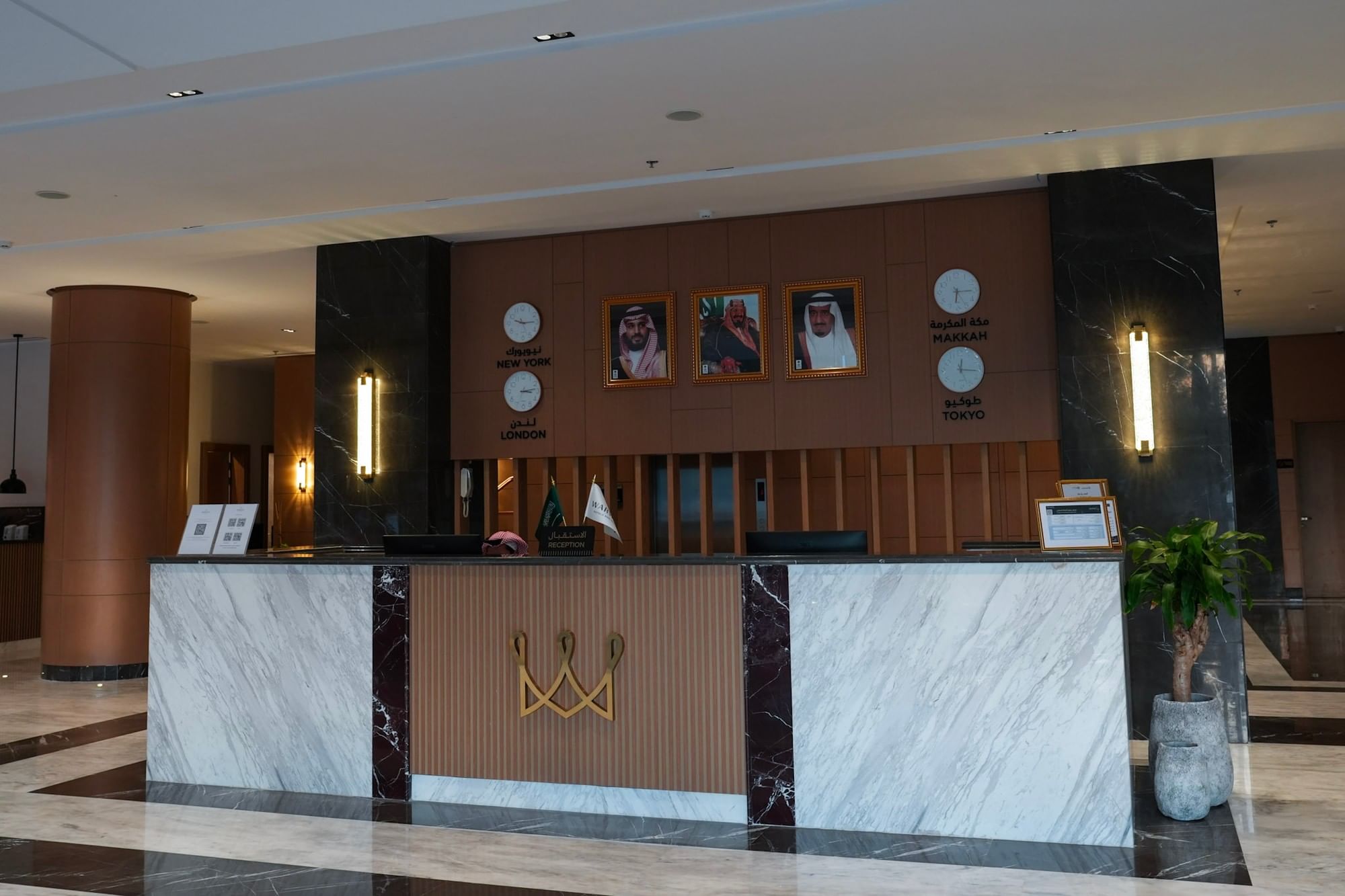 Hotel reception counter with flags, potted plant, and wall with clocks and portraits at Warwick Hotel Spa Jeddah