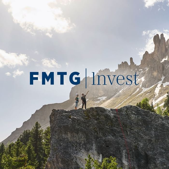 Climbers stand on rocky outcrop with a mountain landscape, and FMTG Invest logo at Falkensteiner Hotels