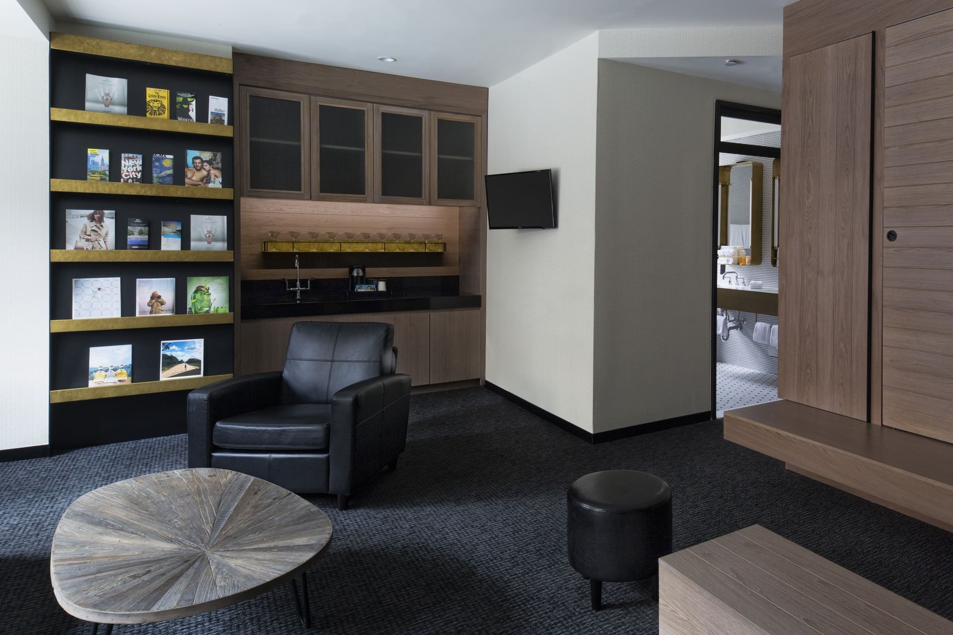 A modern lobby seating area with a bookshelf, leather armchair, coffee table, and flat screen TV.
